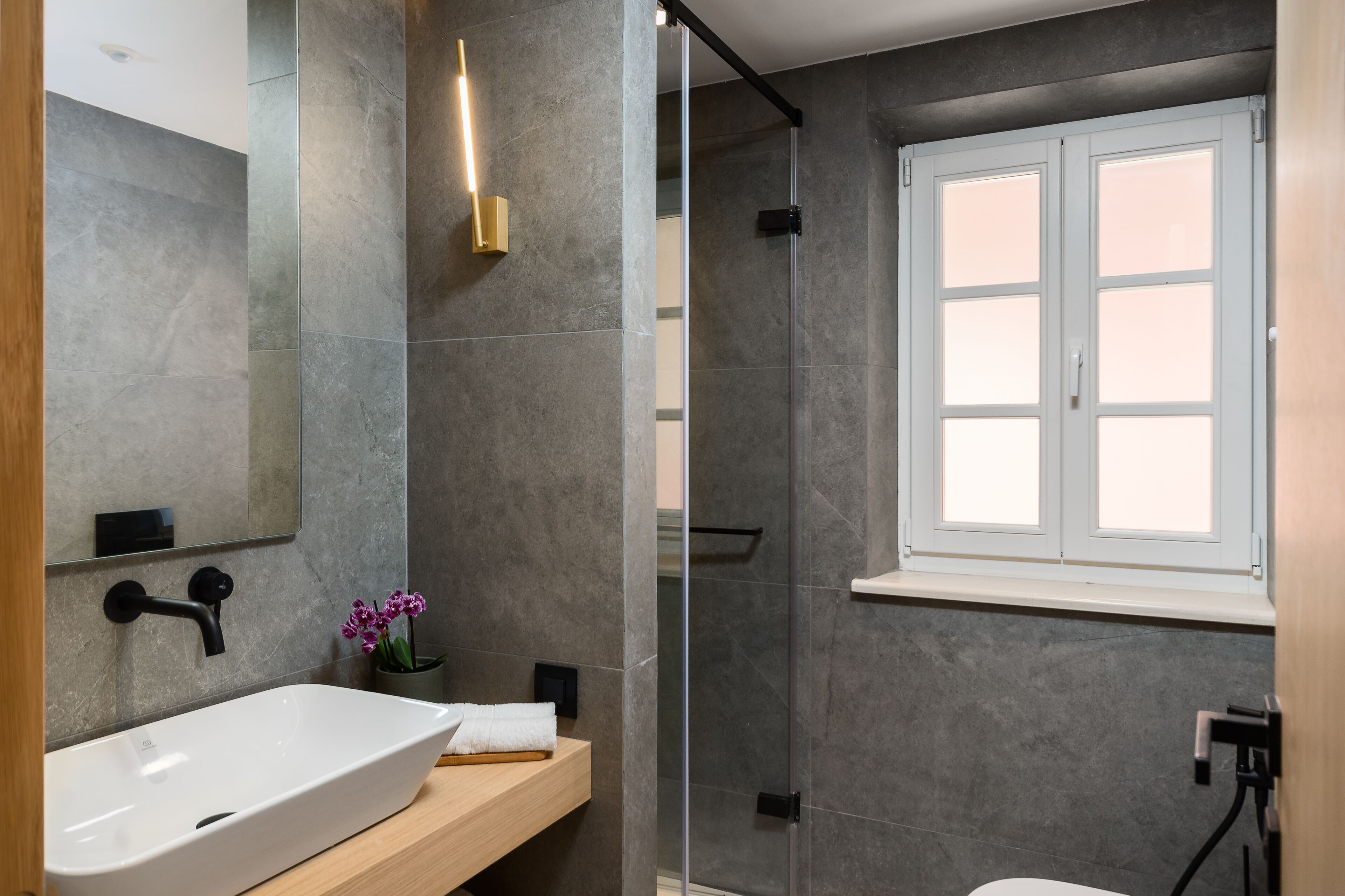 Un baño moderno con un lavamanos grande, cabina de ducha de cristal y ventana.