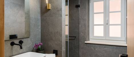A modern bathroom with a large sink, a glass shower enclosure, and a window.