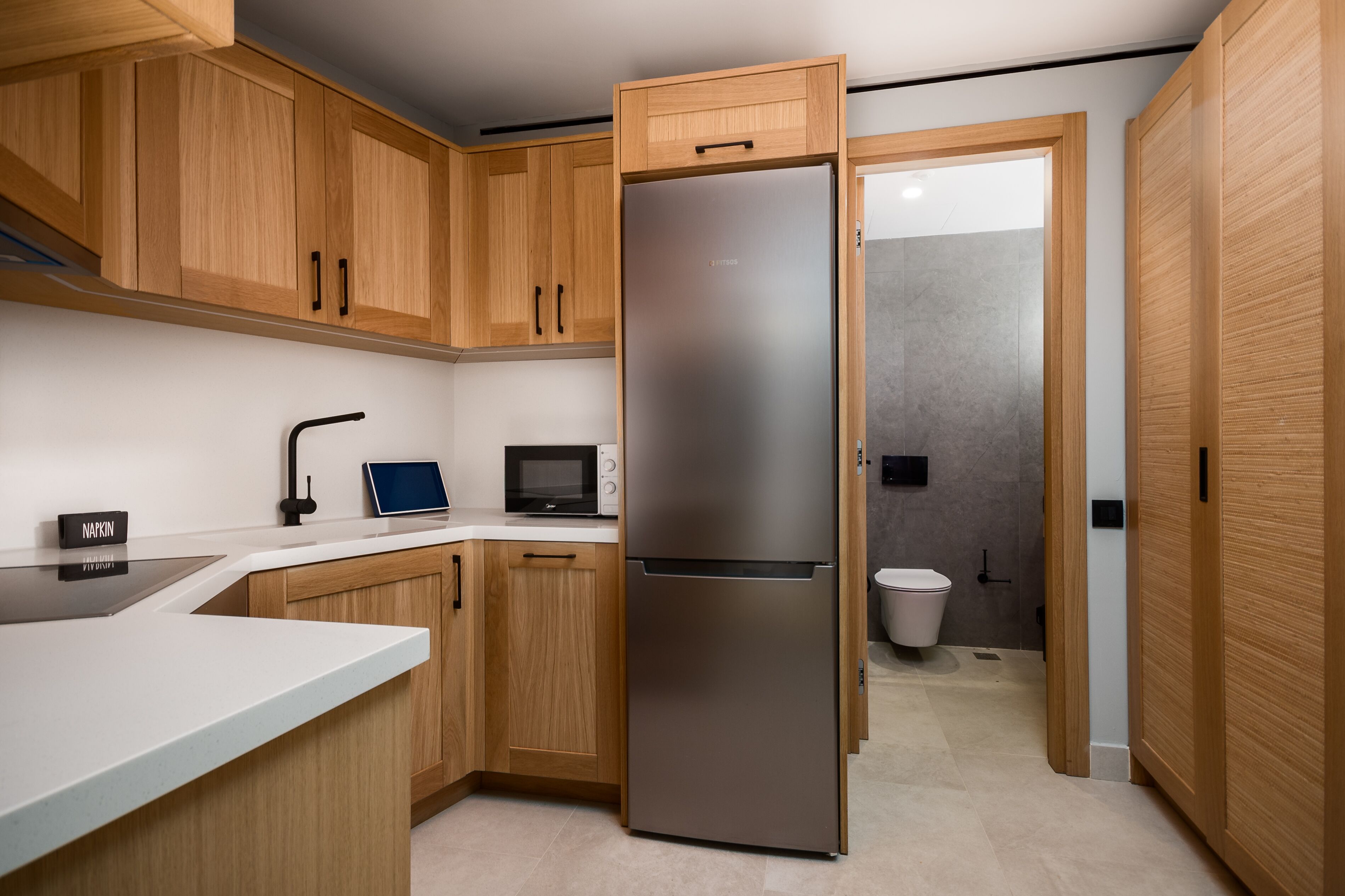 Eine moderne Küche mit Holzschränken, einem Edelstahlkühlschrank, einer Mikrowelle und einem Spülbecken.
