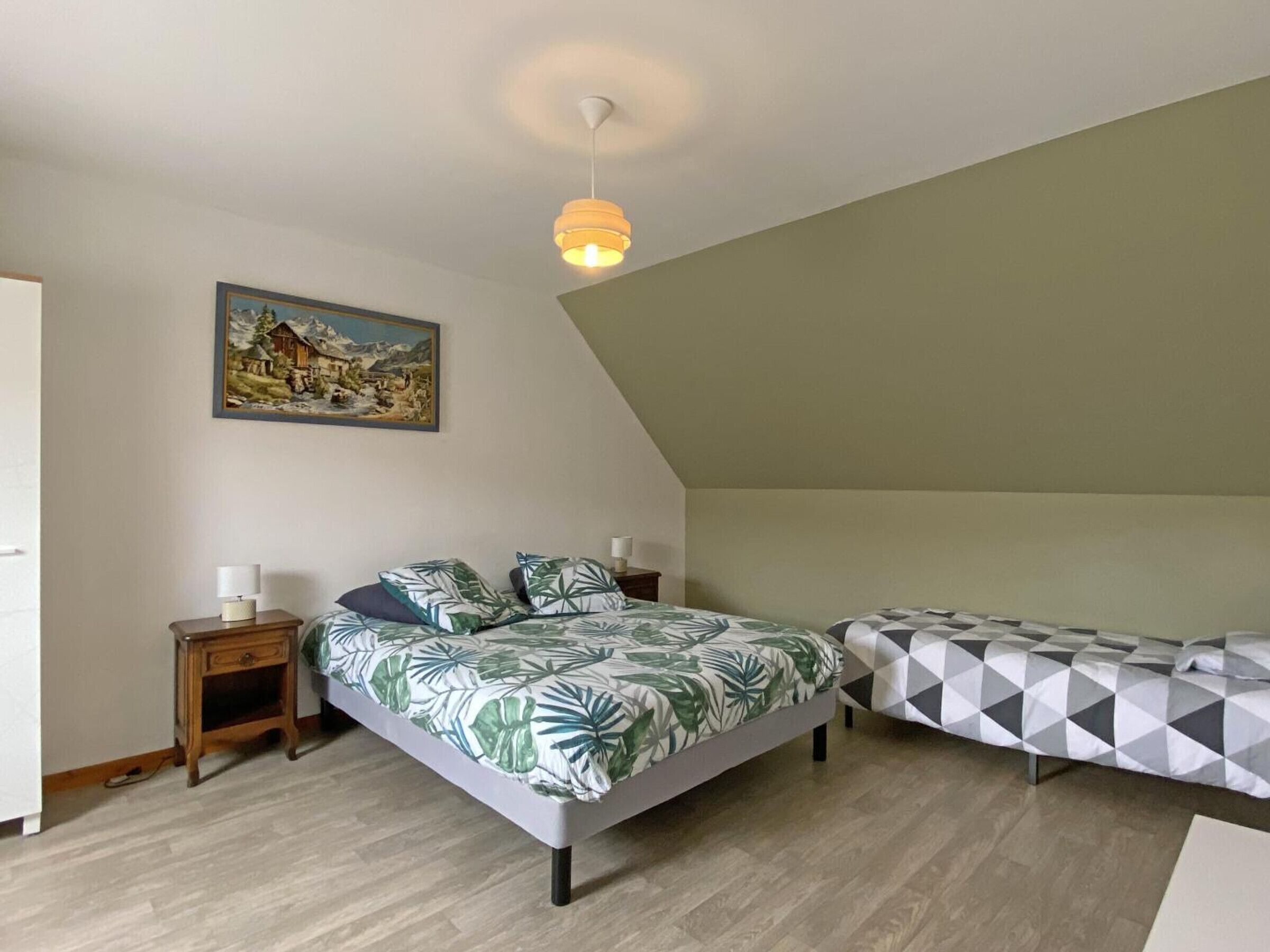 Une chambre à coucher avec un lit, une table de chevet, une lampe, un tableau et un luminaire au plafond.
