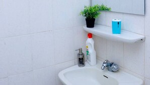 Et badeværelse med en hvid vask, et spejl, en potteplante og en hylde med toiletartikler.
