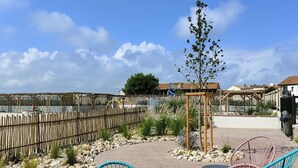 An outdoor patio area with wicker chairs, a small tree, and a wooden pergola. - T2 Apartment with large terrace, parking, pets allowed, and pool (Le Barcarès)