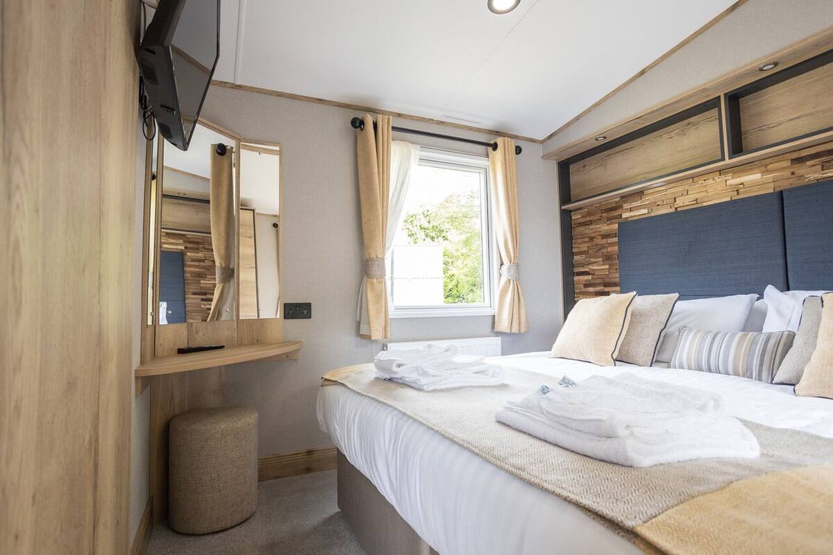 Un dormitorio moderno con cama, mesita de noche, espejo, ventana con cortinas y televisor montado en la pared.