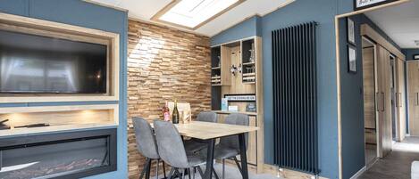 A modern kitchen with a built-in TV, a stone wall, and a dining area with a table and chairs.
