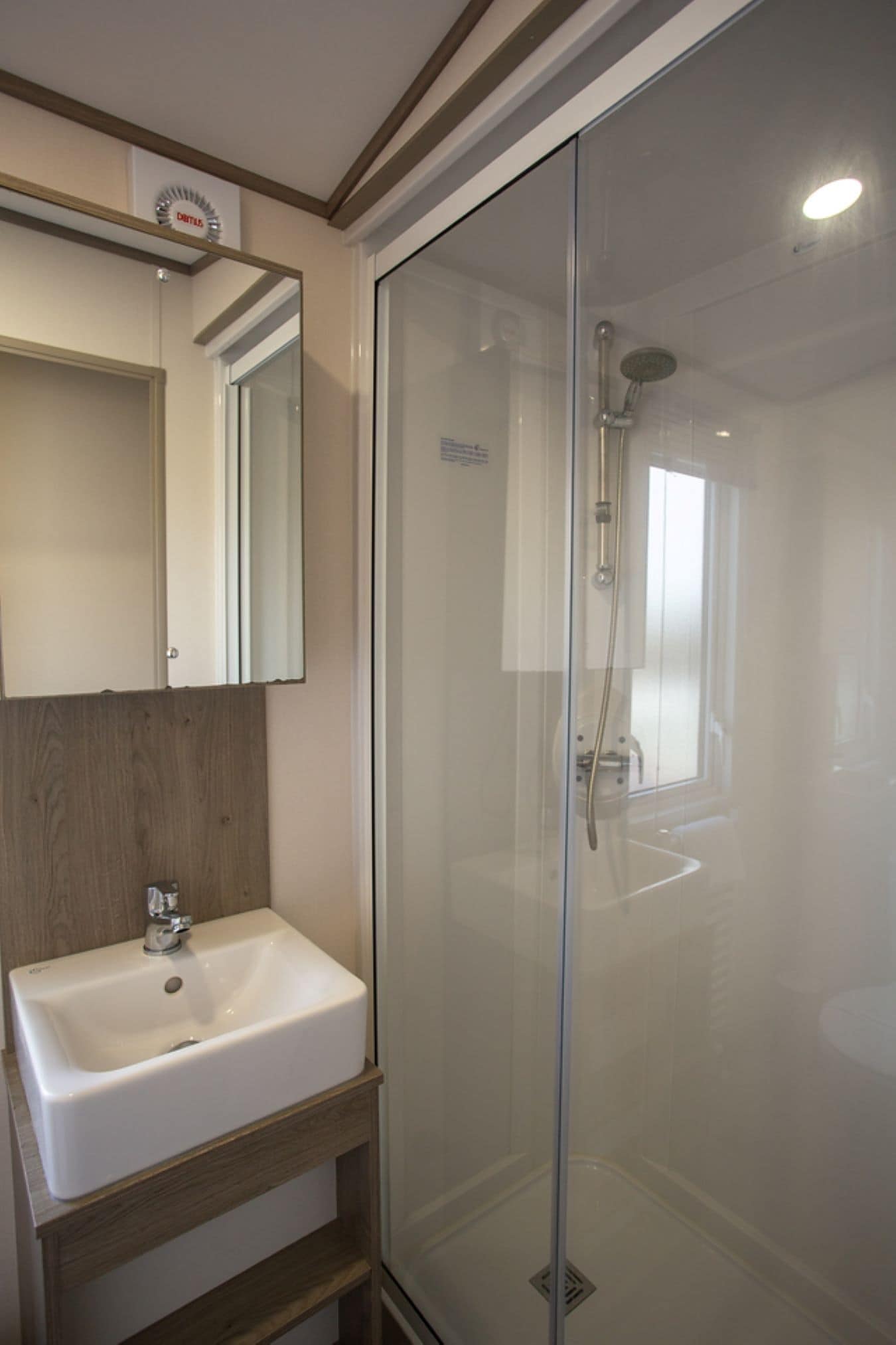 A bathroom with a glass-enclosed shower, a white sink, and a wooden vanity.