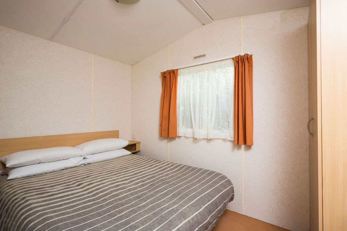 Un dormitorio con cama, mesita de noche, ventana con cortinas y puerta.