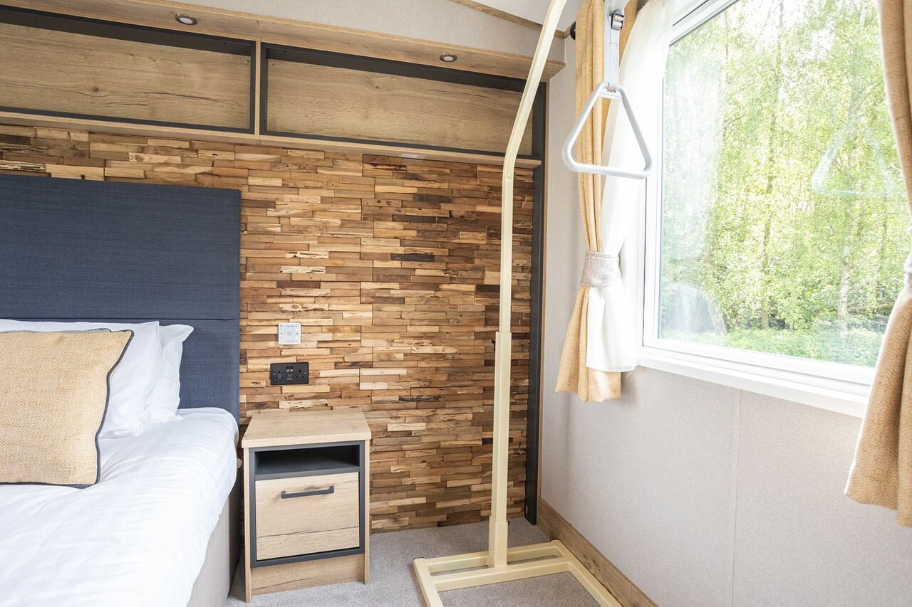 A bedroom with a wooden wall, a bed with white bedding, a bedside table with drawers, and a window with curtains.
