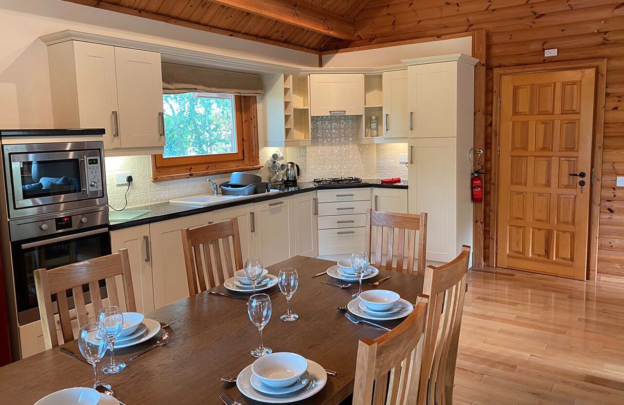Una cocina moderna con armarios blancos, una mesa de comedor de madera preparada para cuatro comensales y un microondas empotrado.
