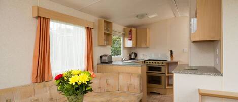 A compact kitchenette with a stove, oven, and sink. There is a small seating area with a bench and a table with a vase of flowers.