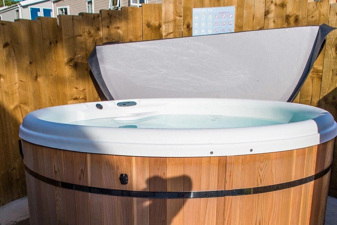 A wooden hot tub with a closed lid, set against a wooden fence.