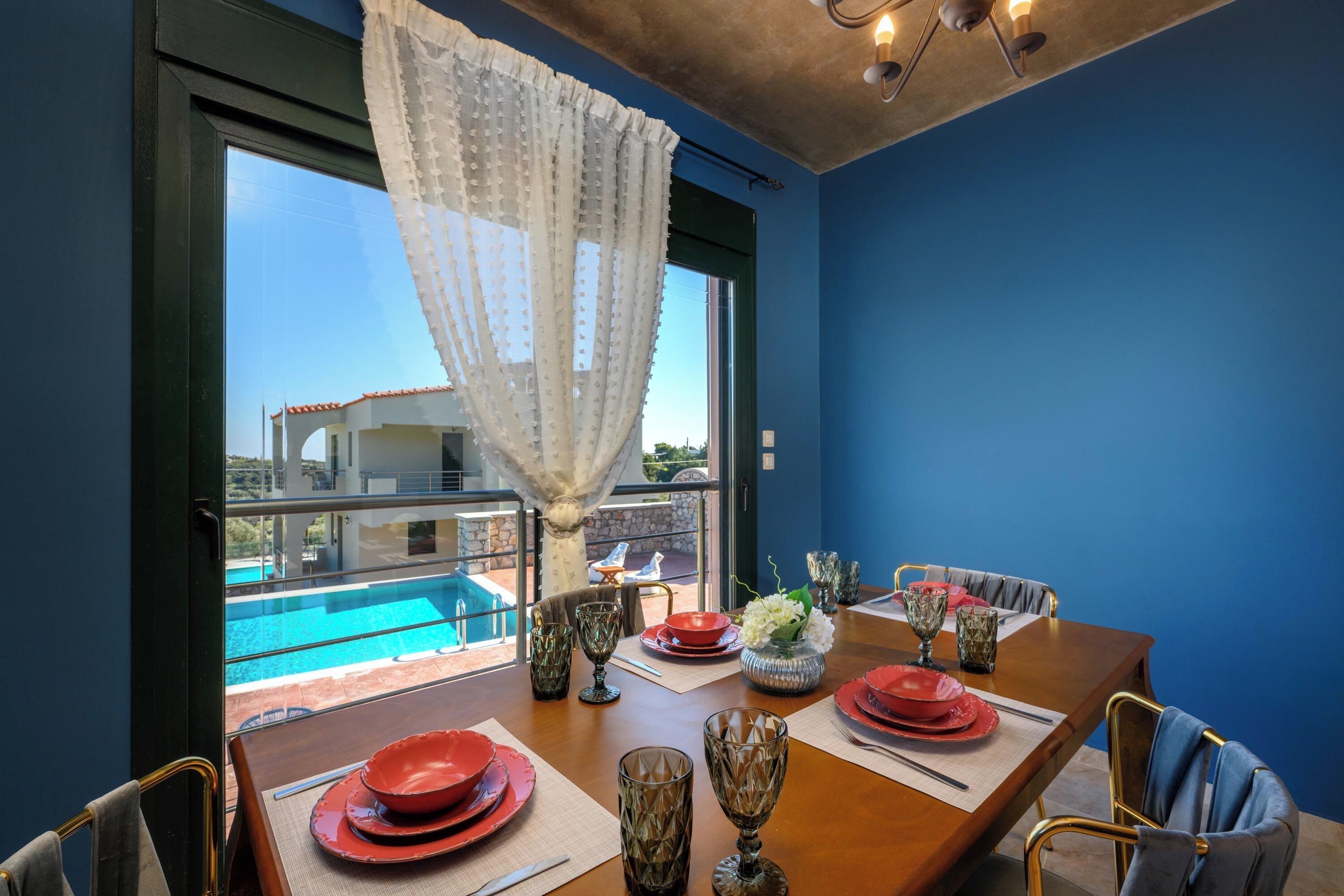 Comedor con una mesa preparada para cuatro, vista a una piscina y un balcón con vistas a un edificio.