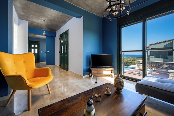 A modern living room with a large window, a flat-screen TV, a wooden coffee table, and a bright orange chair.