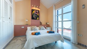 A bedroom with a bed, a nightstand, a wall-mounted lamp, a painting, a window, and a view of the outside. - Holiday Home 'Townhouse beachside Fuengirola' with Shared Pool & Wi-Fi (Fuengirola)