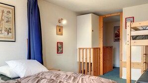 Quarto com uma cama, uma beliche, uma porta e um cartaz na parede.