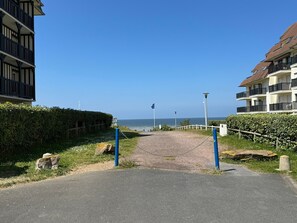 Stroll along the paved pathway to the sea, bordered by a hedge and a fence.