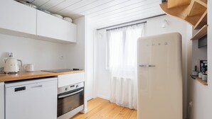 Une cuisine compacte dotée de meubles blancs, d’un lave-vaisselle, d’un four, d’un réfrigérateur et d’un plan de travail en bois.