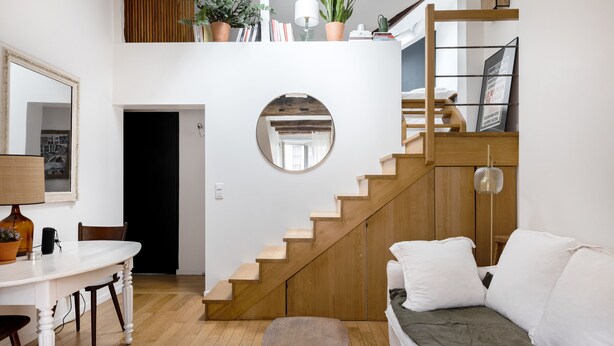 Un espace de vie moderne comprenant un escalier, un grand miroir rond, un coin repas et un canapé.