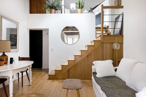 A modern living space with a staircase, a round mirror, a dining area, and a sofa. - In the Eaves of the Écuries, by Veeve (Paris)