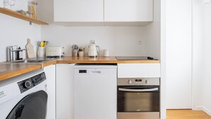 Une cuisine compacte équipée d’un lave-linge, d’un lave-vaisselle, d’un four et d’un plan de travail en bois.
