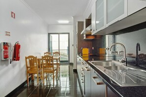 A modern kitchen with a dining area, stainless steel appliances, and a fire extinguisher on the wall. - Apartment Costa Avila 2 with Sea View, Balconies & Wi-Fi (Caniço)