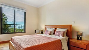 A bedroom with a large window, a bed with a wooden headboard, two bedside tables with lamps, and a view of greenery outside. - Apartment Costa Avila 2 with Sea View, Balconies & Wi-Fi (Caniço)