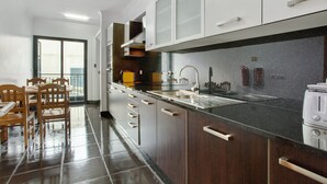A modern kitchen with a dark countertop, white cabinets, and a dining area with wooden chairs. - Apartment Costa Avila 2 with Sea View, Balconies & Wi-Fi (Caniço)