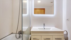 A modern bathroom with a glass shower enclosure, a white sink, and a wooden cabinet. - Apartment Costa Avila 2 with Sea View, Balconies & Wi-Fi (Caniço)