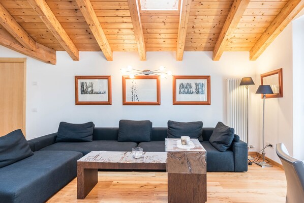 Una sala de estar moderna con techo de madera, un sofá seccional, una mesa de centro y cuadros en la pared.