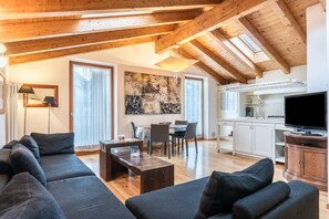 Una sala de estar moderna con techo de madera, un cuadro grande, un comedor y una cocina con televisor.