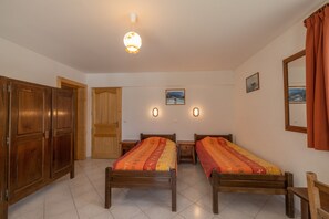Une pièce comprenant deux lits en bois, une armoire en bois, une porte et un luminaire fixé au mur.