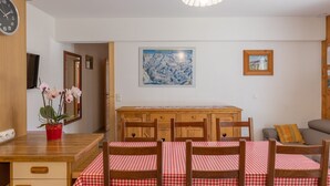 A dining area with a wooden table and chairs, a clock, and a map on the wall. - Apartment 'Le petit chez soi' with Mountain View, Terrace & Wi-Fi (Châtel)