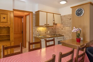 Une cuisine compacte avec des meubles en bois, un évier, une cuisinière et un coin repas agrémenté d’une nappe à carreaux.