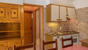 A kitchen with wooden cabinets, a sink, stove, and a table with a checkered tablecloth. - Apartment 'Le petit chez soi' with Mountain View, Terrace & Wi-Fi (Châtel)