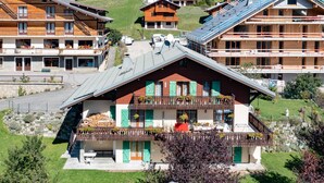 A multi-story building with balconies, a ski slope in the background, and a clear sky. - Apartment 'Le petit chez soi' with Mountain View, Terrace & Wi-Fi (Châtel)
