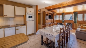 A kitchen with wooden cabinets, a dining table set for four, and a living area with a sofa. - Apartment La Rose des Vents N 3 with Mountain View, Balcony & Wi-Fi (Chatel)