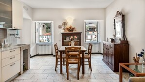 A kitchen with a dining table, chairs, a fireplace, and a view of buildings through the windows. - GuestHost - Cozy 40 sqm studio apartment, accommodating up to 4 people, located on the mezzanine floor of a typical Ligurian home.The property, overlooking the village, is located in Riomaggiore, one of the famous Cinque Terre, about 5 minutes from the t (Riomaggiore)
