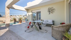 Une terrasse avec une table et des chaises en verre, un canapé en osier et un élément décoratif mural.