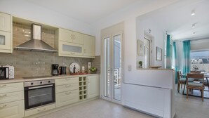 Une cuisine moderne dotée d’appareils électroménagers intégrés, un coin repas avec une table et des chaises, et une vue à travers la porte vitrée.