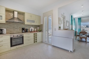 A modern kitchen with built-in appliances, a dining area with a table and chairs, and a view through the glass door.