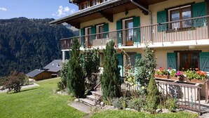 A two-story building with a balcony, surrounded by greenery and mountains. - Apartment 'La Rose des Vents N 1' with Mountain View, Balcony & Wi-Fi (Châtel)