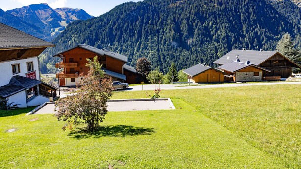 A mountain village with wooden houses, a small parking area, and a view of the surrounding forested mountains. - Apartment 'La Rose des Vents N 1' with Mountain View, Balcony & Wi-Fi (Châtel)