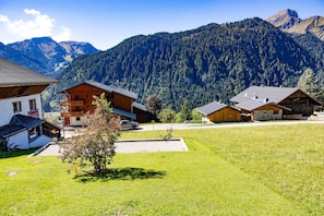 A mountain village with wooden houses, a small parking area, and a view of the surrounding forested mountains.