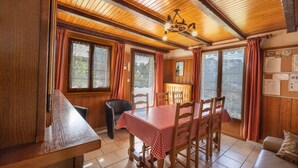 A wooden interior with a dining table, chairs, a sofa, and a view through large windows. - Apartment 'La Rose des Vents N 1' with Mountain View, Balcony & Wi-Fi (Châtel)