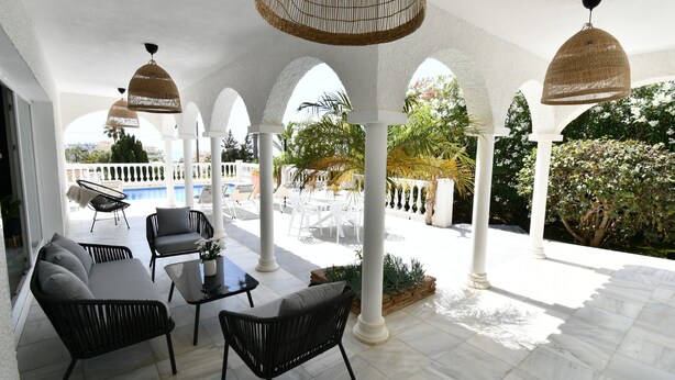 A covered outdoor seating area with white columns, wicker pendant lights, and a pool in the background. - Villa 'With Separate Apartment' near Beach with Pool, Terrace & Wi-Fi (Mijas Costa)