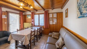 A cozy room with wooden walls, a dining table with chairs, a sofa, and a ceiling with wooden beams and hanging lights. - Apartment La rose des vents N 2 with Mountain View, Balcony & Wi-Fi (Chatel)