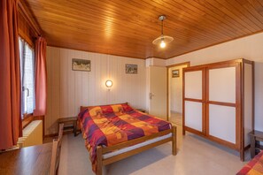 Ein Zimmer mit Holzboden, einem Bett mit farbenfroher Steppdecke, einem Holzschrank und einem Fenster mit Vorhängen.