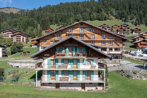 Um hotel com vários andares e varandas, com um teleférico ao fundo e montanhas ao fundo.