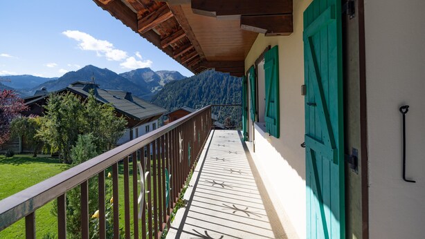 A balcony with a wooden railing, a view of mountains, and a building with green shutters. - Apartment La rose des vents N 2 with Mountain View, Balcony & Wi-Fi (Chatel)