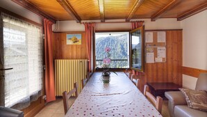 A dining area with a table set for four, wooden walls, a window with a view of mountains, and a bulletin board on the wall. - Apartment La rose des vents N 2 with Mountain View, Balcony & Wi-Fi (Chatel)