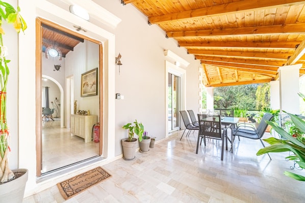 A covered patio area with a wooden ceiling, potted plants, and a dining table with chairs.